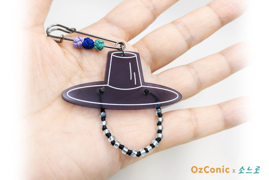 Hand holding a decorative keychain with a hat design and beaded chain.